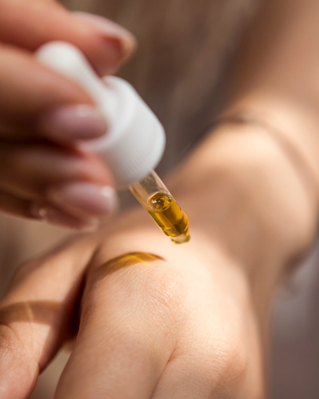A person applying oil to their hand with a dropper 